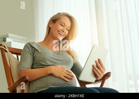 Dont have all the answers Theres an app for that. a pregnant woman using her digital tablet while sitting on a rocking chair. Stock Photo