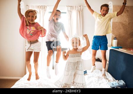 Four little monkeys jumping on the bed. Portrait of little siblings jumping on a bed at home. Stock Photo