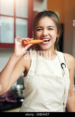 I really do carrot about what I eat. Cropped portrait of an attractive young woman taking a bite of a carrot at home. Stock Photo