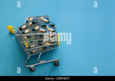 Supermarket trolley filled with pills on a blue background. Purchasing power, medicine and healthcare concept Stock Photo