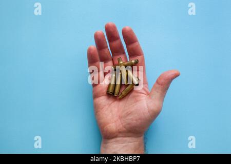 Empty cartridge cases in a male hand on a blue background. Army theme. Military training, fire training. Firearms. Stock Photo