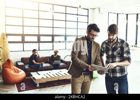 Use technology as part of your creative process. two designers discussing something on a tablet. Stock Photo