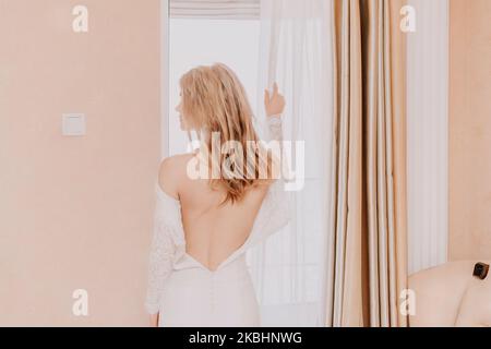 Morning preparation of the bride. Close-up of a bridesmaid, fastening a lot of buttons on the bride's wedding dress. The bride in a white wedding Stock Photo