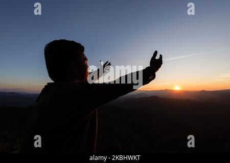 silhouette of a man Praying hands with faith in religion and belief in God On the morning sunrise background.  Prayer position. Stock Photo
