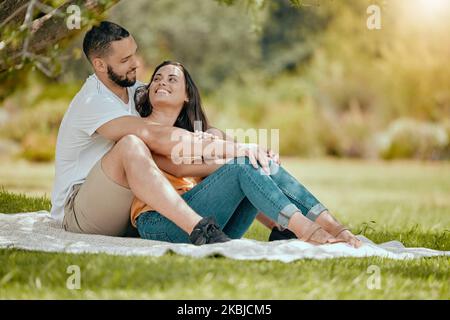 Couple relax on grass, outdoor picnic in park and love sitting on blanket in Miami garden under a tree. Romantic date in spring, woman smile at happy Stock Photo