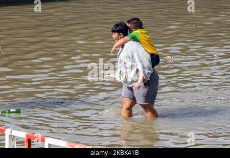 SAMUT PRAKAN, THAILAND, OCT 29 2022, A woman carries a child on her back through a flooded street Stock Photo