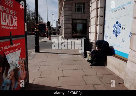 A homeless person sits outside Green Park station on a near-deserted Piccadilly in London, England, on March 21, 2020. Much of central London was virtually empty today, a day after British Prime Minister Boris Johnson ordered the closure of all pubs, bars, cafes and restaurants around the country. The move represents a toughening of measures to enforce the 'social distancing' that is being urged on citizens to reduce the growth of covid-19 coronavirus infections. Nightclubs, theatres, cinemas, gyms and leisure centres were also ordered closed. Some shops in the centre of capital remained open  Stock Photo