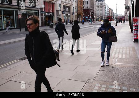 People walk along a near-deserted Oxford Street in London, England, on March 21, 2020. Much of central London was virtually empty today, a day after British Prime Minister Boris Johnson ordered the closure of all pubs, bars, cafes and restaurants around the country. The move represents a toughening of measures to enforce the 'social distancing' that is being urged on citizens to reduce the growth of covid-19 coronavirus infections. Nightclubs, theatres, cinemas, gyms and leisure centres were also ordered closed. Some shops in the centre of capital remained open today, albeit mostly deserted of Stock Photo