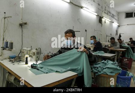 Palestinian workers manufacture protective coverall suits and masks at a workshop in Gaza City on March 31, 2020. amid coronavirus COVID-19 pandemic. Factories in the Gaza Strip used to specialize in the manufacture of shirts and jeans, for despite the closure of many of them in previous years due to the blockade imposed on the Gaza Strip and the inability to export and its aftermath From economic problems that led to the closure of many factories, But with the invasion of the new coronavirus to the world, some factories returned to work in medical clothing, and lines of men and women used old Stock Photo