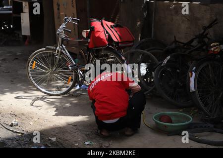 A Zomato Food delivery boy repairs his bicycle amid Covid-19 (Coronavirus) lock down in Gurugram on the Outskirts of New Delhi, India on 07 April 2020. To combat the spread of deadly COVID-19, PM of India Narendra Modi has recently announced a 21-day lockdown. However, the curfew-like situation has forced migrant workers to return to their homes when traffic is entirely off the roads apart from the railway and air traffic. So much so, many workers are left stranded with no food, shelter and other necessities. The lockdown has also enforced multi-national companies to fire thousands of employee Stock Photo