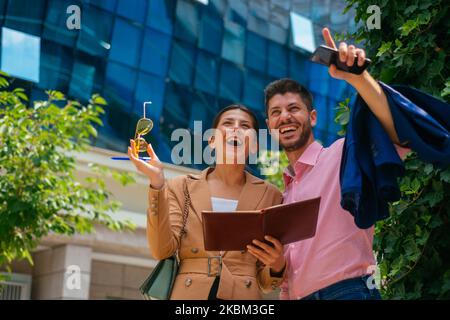 A happy male businessman is pointing somwhere and makes his female colleague laughing Stock Photo