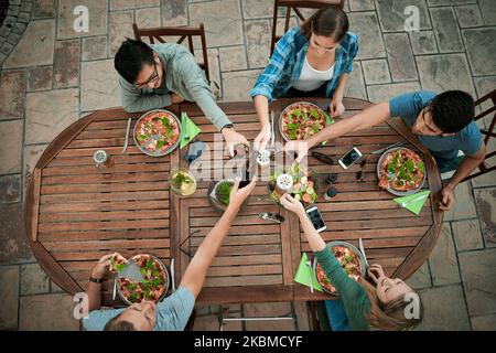 We are a circle of friends. High angle shot of a group young friends holding drinks and toasting together outside around a table. Stock Photo