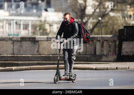 A food delivery worker driving electric scooter wears a protective face mask due to the spread of coronavirus. Krakow, Poland on April 16, 2020. The rule of covering the nose and mouth in public places with face masks, carves or handkerchiefs came into force from April 16th. The order will not apply to children up to the age of two and people who are unable to cover their mouth or nose due to breathing difficulties. (Photo by Beata Zawrzel/NurPhoto) Stock Photo