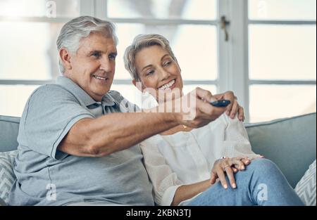 Senior couple, smile and hug watching TV for entertainment on living room sofa with remote at home. Happy elderly man and woman relaxing on couch Stock Photo