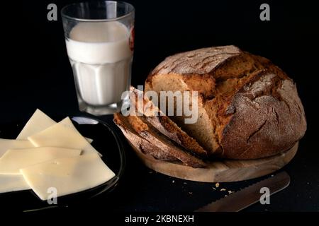 photo of sliced fresh bread on a wooden kitchen board with a glass of milk and cheese Stock Photo