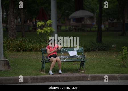 A woman is seen without face mask sits on a bench next to a marked sign for social distancing measure at Lumphini public park before starting night curfew on May 8, 2020 in Bangkok, Thailand. As Thai government allowanced to an easing of measures to combat the spread of the coronavirus after Thailand's lockdown was partially lifted and the number of new infections continues to decline. (Photo by Vachira Vachira/NurPhoto) Stock Photo