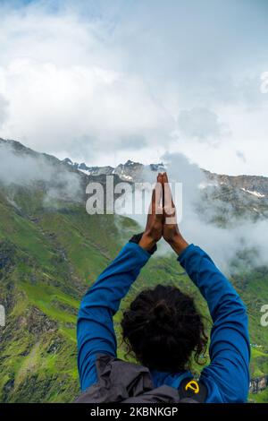 July 14th 2022, Himachal Pradesh India. A man holding an overhead Namaste pose with folded hands towards Shrikhand Mahadev Peak, the Shivling, a symbo Stock Photo