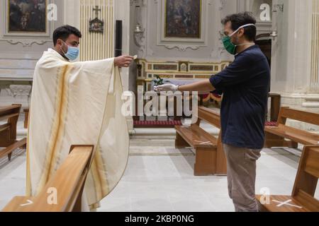 The priest with mask and gloves prepares to give Communion on the hands of the faithful covered with gloves, in Carolei (CS) on May 18, 2020. Churches reopen in Italy on May 18, 2020. After more than two months of lockdown, the government has given the green light to 'phase 2' or the reopening of churches and general stores. (Photo by Andrea Pirri/NurPhoto) Stock Photo