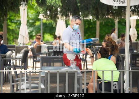 A waiter sanitizes a table surface for young customers at the outdoor terrace of a cafe in Madrid, Spain on May 25. Today is the first day of Madrid in phase 1 of the confinement de-escalation, people can go to terraces and terraces and can start to stay with groups of more than 10 people, Parque del Retiro, Madrid. (Photo by Jon Imanol Reino/NurPhoto) Stock Photo