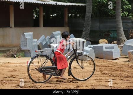 Tamil girl rides her bicycle past large stones waiting to be carved during re-construction of the Raja Gopuram tower of the Arul Eswari Muthumariamman Hindu temple in Jaffna, Sri Lanka on August 15, 2017. The tower was destroyed by bombing during the 26-year long civil war between the Sri Lankan Army and the LTTE (Liberation Tigers of Tamil Eelam). This is just one of the many reminders of the deep scars left behind by the civil war that killed an estimated 40,000 people. (Photo by Creative Touch Imaging Ltd./NurPhoto) Stock Photo