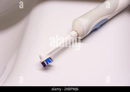 A worn and dirty electric toothbrush is lying on the white sink, top view Stock Photo