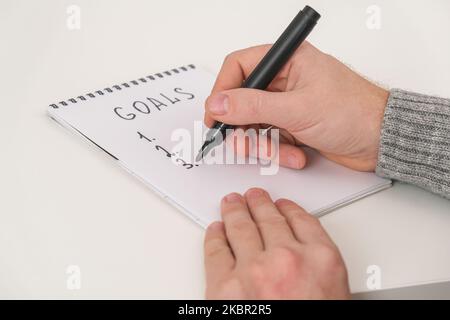 Man writes marker board at white table with Christmas decor goals and plans new year and Christmas. Goals New Year and Christmas written marker board. List wishes and goals new year and Christmas 2023 Stock Photo