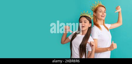 Mother and daughter child banner, copy space, isolated background. Happy woman and girl kid in crowns point fingers at promotional tshirts for copy Stock Photo