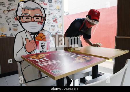 Waiters tidy up tables and draw KFC (Kentucky Fried Chicken) characters around tables and benches, in Salemba, Jakarta, on June, 24,2020. The character banner is used as a barrier for visitors who eat on the spot during the new normality phase. (Photo by Dasril Roszandi/NurPhoto) Stock Photo