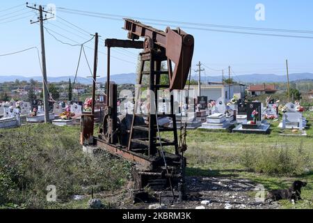 ALBANIA, Kuçova, named Stalin city from 1950 to1991, crude oil field and old drilling pump at cemetery, still operating and polluting the environment / ALBANIEN, Kucova, von 1950 bis 1991 Qyteti Stalin, Stalinstadt, Erdoelfoerderung, alte Oelfoerderpumpe, die heute noch zur Ölförderung in Betrieb sind, an einem Friedhof Stock Photo