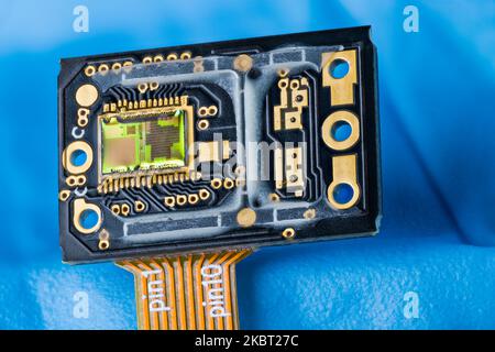 Optoelectronic image sensor of optical laser computer mouse on a blue background. Modern green silicon die on printed circuit board. Orange flex cable. Stock Photo