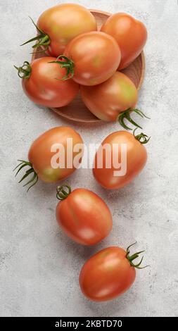 ripe tomatoes on a wooden plate with scattered on white textured surface, edible berries taken from above Stock Photo