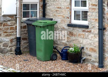 A Green and a black wheelie bin in front of a house entrance somewhere in a small village near Leyburn, Yorkshire, UK. Stock Photo
