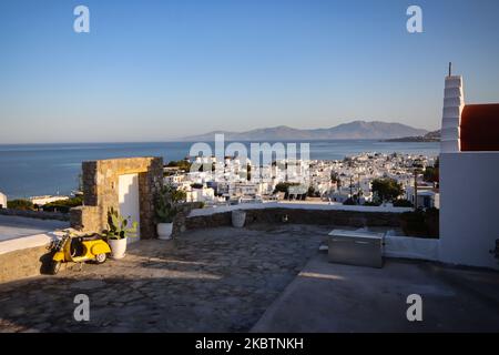 Early morning panoramic view of the windmills and Mykonos Town, the overview is seen from a hill with a Vespa scooter motorcycle and a traditional chapel. The iconic windmills in Mykonos island, Cyclades islands, Aegean Sea, Greece on July 14, 2020. There are 16 windmills on the island, 5 of them above Chora or Mykonos Town, the main town on the island. The windmills were built in the 16th century from the Venetians but their constructions continued until the 20th century. The famous Mediterranean Greek island is nicknamed as The Island of the Winds with whitewashed traditional buildings like  Stock Photo