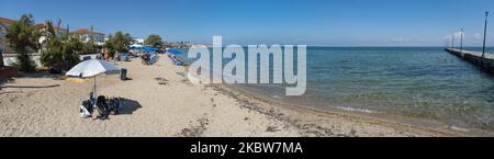 Panoramic view of the beach and the promenade. Everyday life at the sandy beach of Agia Triada near Thessaloniki in Greece on July 26, 2020. Agia Triada is a summer tourist destination for locals and foreign tourists for holidays mostly from the Balkan countries. The beach is awarded with Blue Flag, has typical for Greek Beaches and the Aegean Sea, crystal clear transparent sea water, golden sand and many tourism facilities such as a pedestrian waterfront road next to the shore, free showers etc. There are hotels, taverns, restaurants, bars and beach bars in the area, which is just a few minut Stock Photo