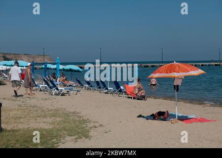 Everyday life at the sandy beach of Agia Triada near Thessaloniki in Greece on July 26, 2020. Agia Triada is a summer tourist destination for locals and foreign tourists for holidays mostly from the Balkan countries. The beach is awarded with Blue Flag, has typical for Greek Beaches and the Aegean Sea, crystal clear transparent sea water, golden sand and many tourism facilities such as a pedestrian waterfront road next to the shore, free showers etc. There are hotels, taverns, restaurants, bars and beach bars in the area, which is just a few minutes driving away from Thessaloniki International Stock Photo