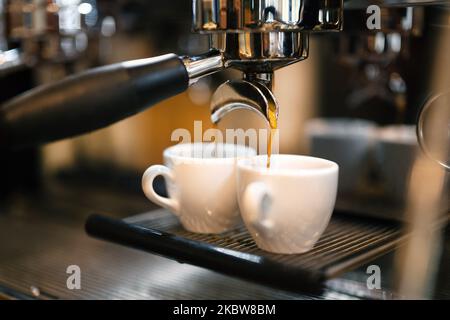 Espresso coffee flows from a portafilter coffee machine into two white espresso cups. Stock Photo