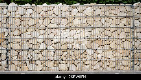 Light beige natural stones are neatly layered in a galvanized gabion wall. Stock Photo