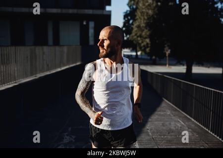 Bearded tattooed man jogging outdoors, portrait of athletic guy making cardio training in the city Stock Photo