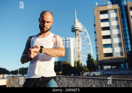 Tattooed young man using new sports watch on jogging run checking his heart rate, using modern tech gadget for fitness health active lifestyle Stock Photo