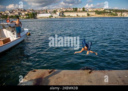 People jump into the Bosphorus to cool off as he enjoy the warm weather during the second day of the celebrations of the Eid-al-Adha in Istanbul, Turkey, 01 August 2020. Eid al-Adha is the holiest of the two Muslims holidays celebrated each year, it marks the yearly Muslim pilgrimage (Hajj) to visit Mecca, the holiest place in Islam. Muslims slaughter a sacrificial animal and split the meat into three parts, one for the family, one for friends and relatives, and one for the poor and needy. (Photo by Fayed El-Geziry/NurPhoto) Stock Photo