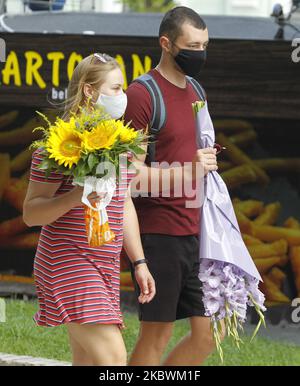 Young people wearing protective masks amid the Covid-19 coronavirus epidemic carry flowers on a street in center of Kyiv, Ukraine, on 03 August, 2020. New rules of adaptive quarantine due the COVID-19 coronavirus spread shall be applied in Ukraine, the country's cities and districts are divided into 4 zones depending on the epidemiological situation, as local media reported. (Photo by STR/NurPhoto) Stock Photo