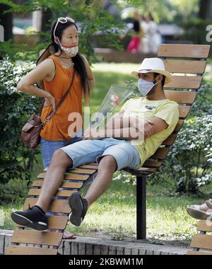 Young people, wearing protective masks amid the Covid-19 coronavirus epidemic, rest on a bench at a park in center of Kyiv, Ukraine, on 03 August, 2020. New rules of adaptive quarantine due the COVID-19 coronavirus spread shall be applied in Ukraine, the country's cities and districts are divided into 4 zones depending on the epidemiological situation, as local media reported. (Photo by STR/NurPhoto) Stock Photo
