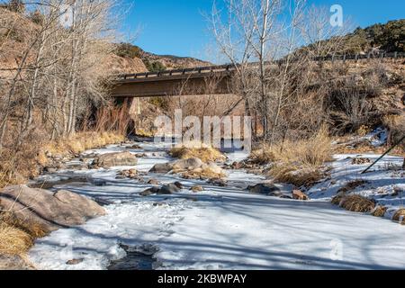An ice covered mountain stream flows beneath a bridge crossing in a southern Colorado canyon. Stock Photo