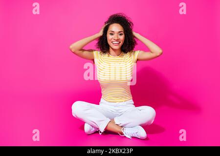 Full size photo of young adorable nice girl sitting touch hair chevelure positive excited good mood summer isolated on pink color background Stock Photo