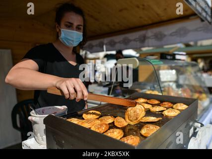 A lady turns a smoked cheese (Polish: Oscypek, a cheese made of salted sheep milk exclusively in the Tatra Mountains) on a grill. The 44th edition of the International Folk Art and Craft Fair takes place in Krakow's Main Market Square, a beautiful tradition and meeting with traditional potters, lace-makers, folk sculptors, weavers, embroiderers, painters, sculptors and blacksmiths from Poland and neighboring countries. On Friday, August 14, 2020, in Krakow, Poland. (Photo by Artur Widak/NurPhoto) Stock Photo