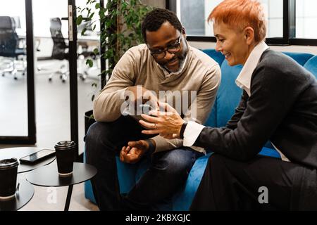 Two multiracial colleagues talking and using cellphone while working in office Stock Photo