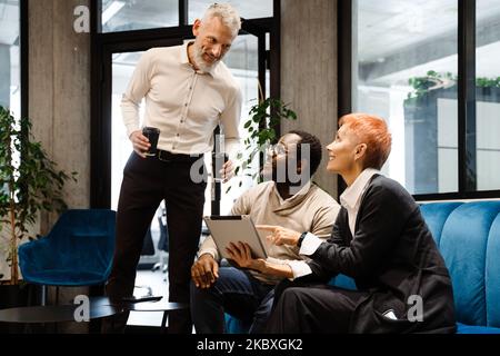 Two multiracial colleagues talking and using cellphone while working in office Stock Photo