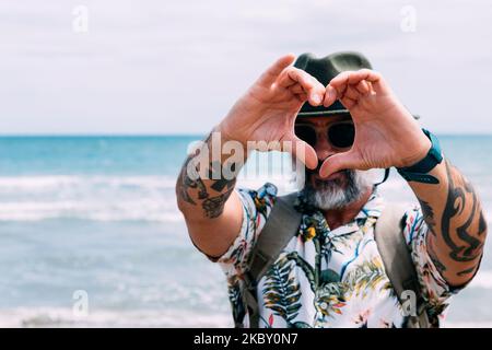 A smiling man making a heart shape with his hands on the beach Stock Photo