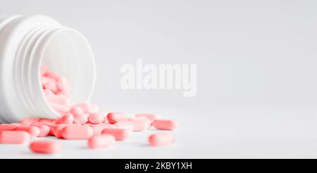 Pink pills with spilled out of a plastic jar. Medicine capsules on white background with copy space. Stock Photo