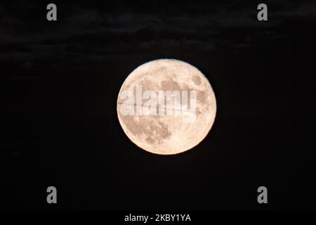 An aircraft passing in front of the full moon in a distance. The Full Corn Moon as seen behind Hortiatis mountain over the city of Thessaloniki in Northern Greece, captured from Kalochori Lagoon and National Park. Earth's natural satellite as seen yellow and then bright illuminating and creating reflections on the seawater. The Lunar phase, Corn Moon happens once every three years and is also known as Fruit Moon, Barley Moon, Hungry Ghost Moon, Binara Pura Pasalosvaka Poya Day, Honey Full Moon for Buddhists etc. Thessaloniki, Greece on September 2, 2020. (Photo by Nicolas Economou/NurPhoto) Stock Photo